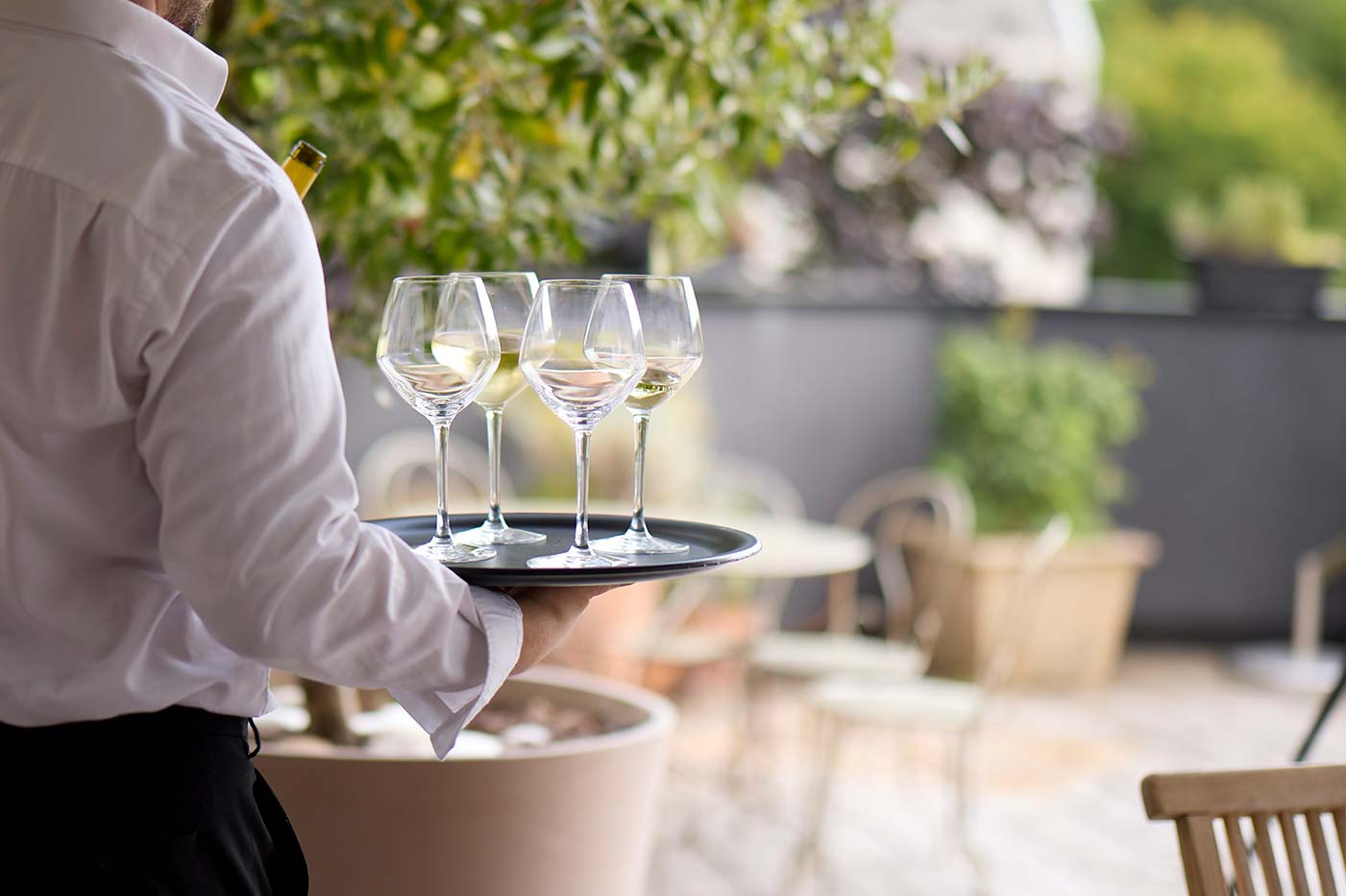 Un serveur vu de dos tient un plateau avec plusieurs verres à vins remplis dessus